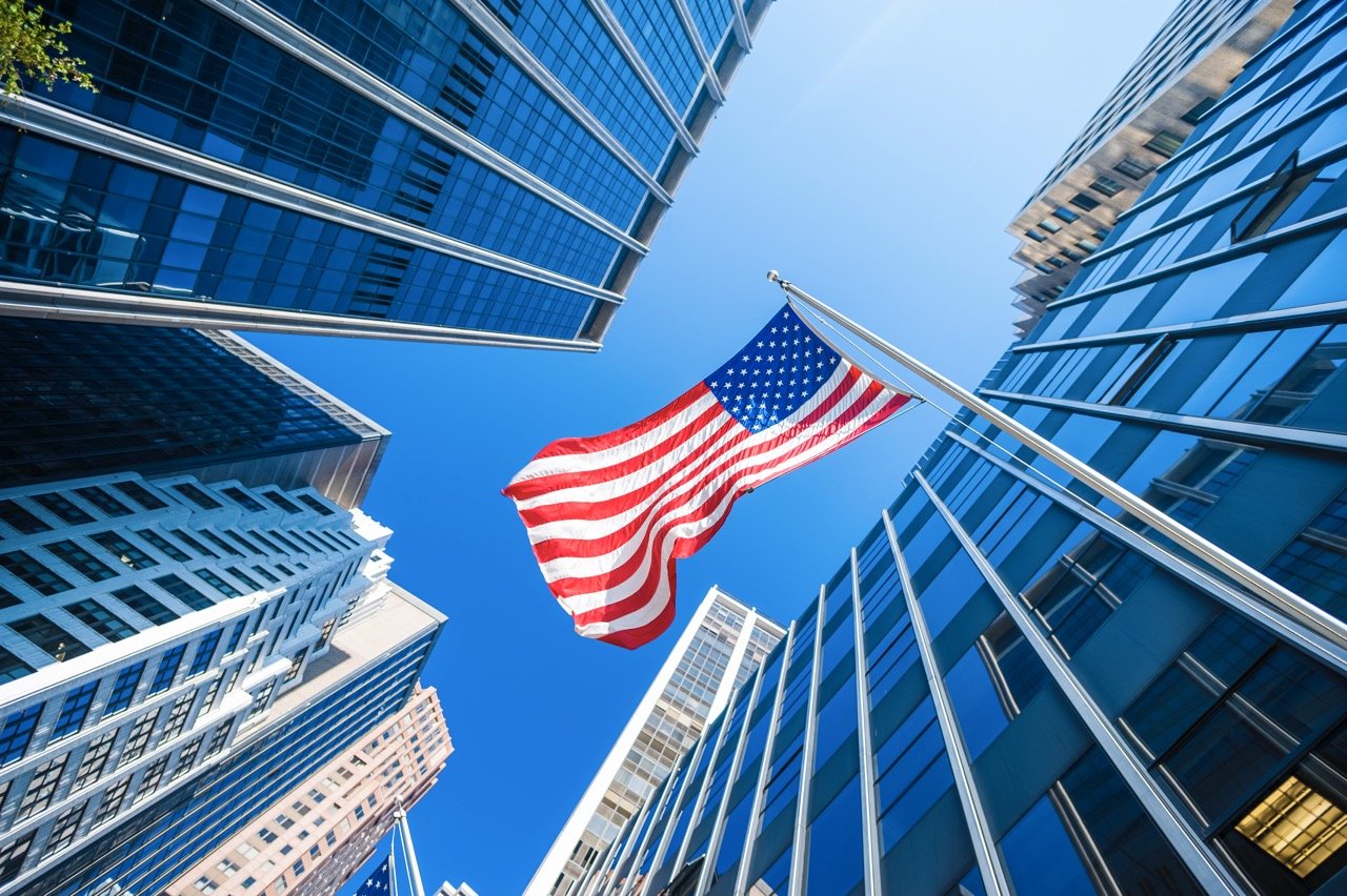 Rascacielos y bandera de Estados Unidos: razones para invertir en una franquicia en EE. UU.